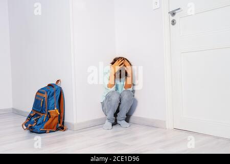 Portrait d'un triste garçon stressé intimidé dans le cri de l'école assis dans le coin avec un sac à dos pour fils Banque D'Images