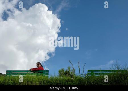 Une belle jeune femme en robe rouge s'asseoir sur un banc vert dans un parc de montagne dans un matin ensoleillé Banque D'Images