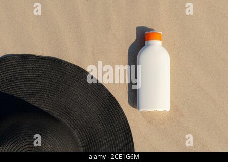 Crème solaire à côté d'un chapeau noir sur le sable lors d'une journée ensoleillée à la plage. Cosmétique de protection des proches pour les bains de soleil. Personne Banque D'Images