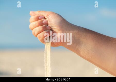 Gros plan sur le sable qui coule de la main sur la plage par une belle journée d'été. Jouer avec le sable en vacances. Banque D'Images