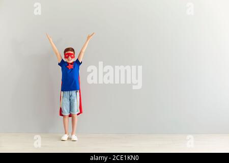 Garçon souriant en costume de super-héros debout avec les mains levées sur fond gris Banque D'Images