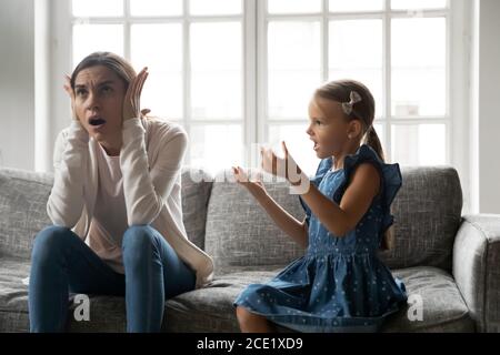 Jeune femme stressée couvrant les oreilles ignorant petite fille méchanceuse. Banque D'Images