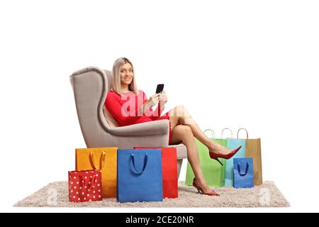 Jeune femme dans un fauteuil avec un téléphone portable et sacs d'achats isolés sur fond blanc Banque D'Images