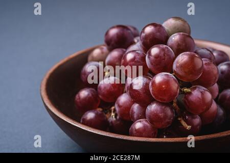 Baies de raisin mûres fraîches dans un bol en bois brun sur fond bleu gris minimal, vue en angle macro Banque D'Images