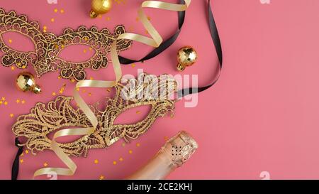 Concept de mascarade de fête de Noël. Bouteille de champagne, masques de carnaval dorés, balles, confettis sur fond rose. Flat lay, vue de dessus. Banque D'Images