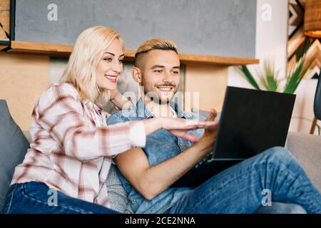 Jeune couple joyeux avec un ordinateur portable surfant sur Internet canapé Banque D'Images