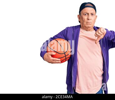 Senior beau gris-cheveux homme tenant le ballon de basket-ball avec le visage en colère, signe négatif montrant l'aversion avec les pouces vers le bas, concept de rejet Banque D'Images