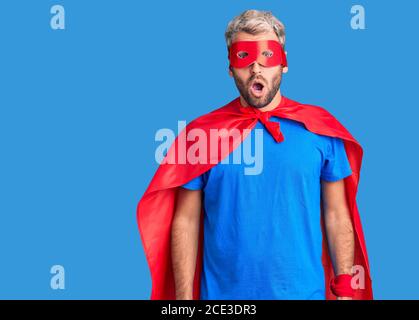 Jeune homme blond portant le super héros crème peur et choqué avec l'expression surprise, la peur et le visage excité. Banque D'Images