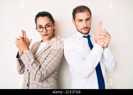 Beau couple portant des vêtements d'affaires tenant un pistolet symbolique avec un geste de main, jouant tuant des armes de tir, visage en colère Banque D'Images