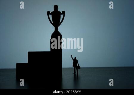Photo conceptuelle de la stratégie d'affaires - Silhouette de l'homme d'affaires miniature pointant sur la victoire du trophée sur le podium Banque D'Images