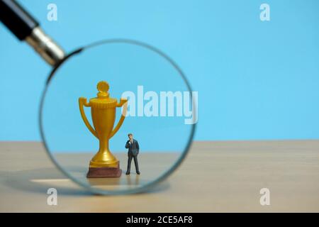 Concept d'affaires miniature - homme d'affaires debout devant l'or verre de trophée et de loupe Banque D'Images