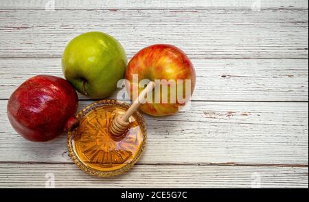 Produits traditionnels pour la célébration de Rosh Hashanah - pommes, grenade, miel, chelins - sur fond de bois blanc Banque D'Images