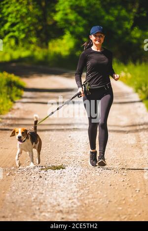 Sport fille est en train de courir avec un chien (Beagle) au printemps ensoleillé jour sur le chemin de la forêt. Banque D'Images