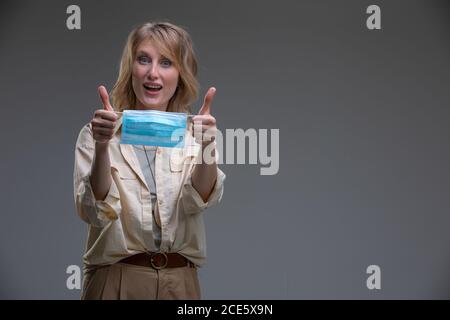 Tête portrait belle blonde femme regardant l'appareil photo tenir médical ou masque chirurgical de couleur bleue Banque D'Images