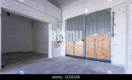 Intérieur de bâtiment industriel avec murs en briques blanches, sol en béton, portes hautes et espace vide pour l'exposition de produits ou l'arrière-plan industriel Banque D'Images