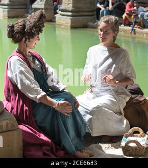 Deux femmes en costume romain assis sur le bord du Grand bain romain, Bath, Angleterre. Des femmes dans des conversations animées. Coiffure extrême. Banque D'Images