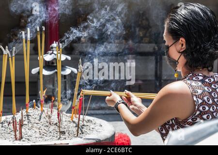 Femme asiatique portant un masque médical pour se protéger de l'infection virale. Brûle des bâtonnets d'encens dans un temple chinois. Masque pour se protéger de cor Banque D'Images