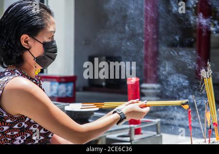 Femme asiatique portant un masque médical pour se protéger de l'infection virale. Brûle des bâtonnets d'encens dans un temple chinois. Masque pour se protéger de cor Banque D'Images