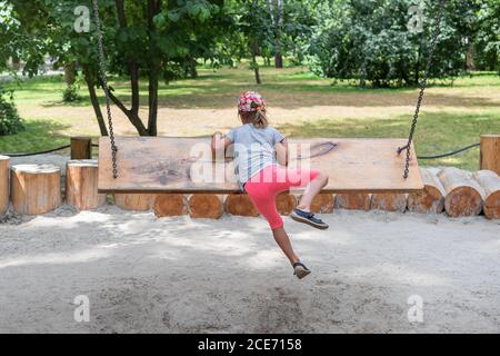 l'enfant essaie de grimper sur un banc - balançant, levant sa jambe vers le haut, vue arrière Banque D'Images