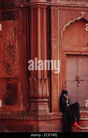Inde - 9 novembre 2012 : une femme ethnique méconnaissable dans des vêtements traditionnels, assise près d'un bâtiment ornemental en ville et ayant une conversation sur un téléphone portable Banque D'Images