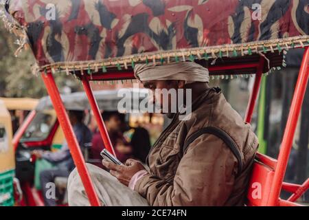 Inde - 9 novembre 2012 : vue latérale d'un homme indien utilisant un smartphone assis en pousse-pousse sur la route de la ville Banque D'Images