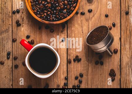 Vue de dessus de la délicieuse boisson dans la tasse placée sur la table avec grains de café et café moulu dans un filtre en métal Banque D'Images