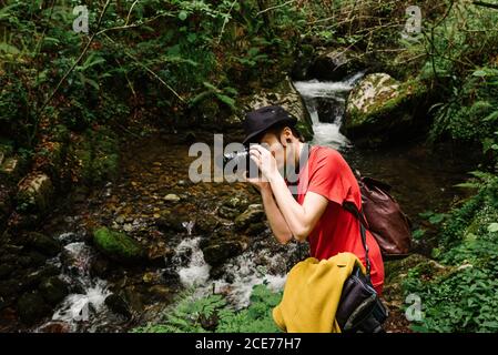 Vue latérale d'une femme de voyage informelle prenant des photos de la nature sur un appareil photo professionnel dans les bois pendant les vacances Banque D'Images