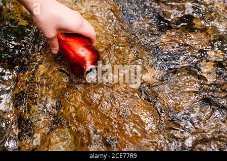 Du dessus de la récolte une femme assoiffée et méconnaissable en vêtements d'extérieur l'eau du ruisseau tout en se reposant dans la forêt verte Banque D'Images