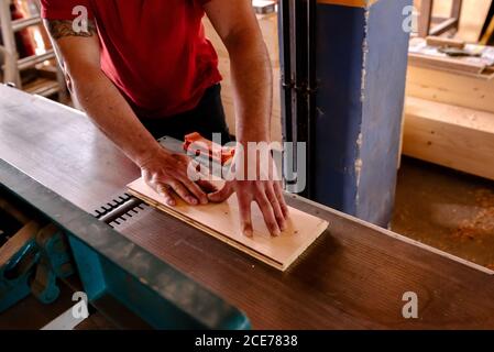 Grand angle de menuiserie anonyme mâle debout à l'établi avec bois de charpente tout en travaillant dans un atelier de merde Banque D'Images