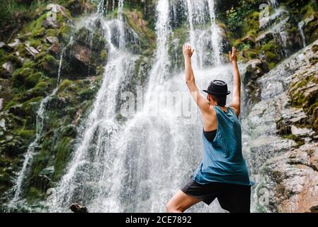 Vue arrière à angle bas de la femelle anonyme sur laquelle se tient le touriste rock et profiter de la cascade étonnante pendant les vacances Banque D'Images