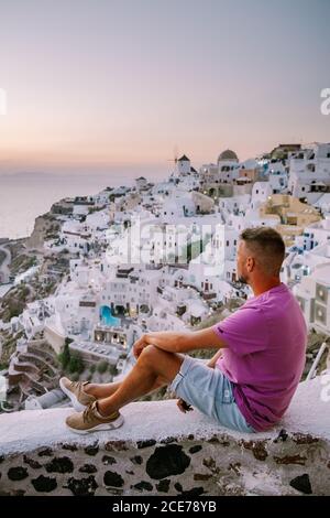 Jeunes hommes regardant le coucher du soleil Santorini Grèce, jeune couple en vacances de luxe à l'île de Santorini regardant le lever du soleil à côté de l'église dôme bleu et Banque D'Images