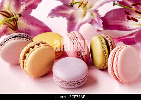 Gros plan de délicieux macarons assortis placés sur une table rose avec fleurs de nénuphars fraîches Banque D'Images