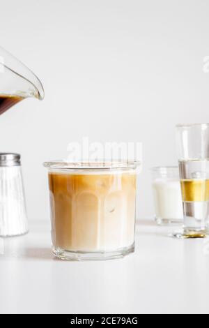 Délicieux latte de café glacé servi dans une tasse de verre sur blanc table avec tasse de lait et verrerie Banque D'Images