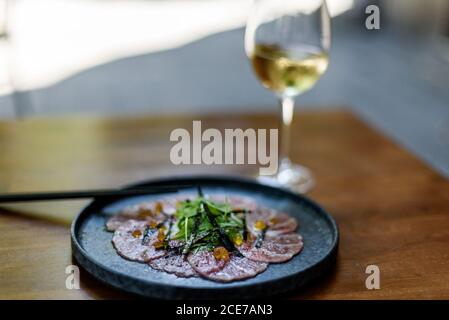 Du dessus des tranches de carpaccio sur l'assiette garni avec des herbes vertes dans le café sur fond noir Banque D'Images