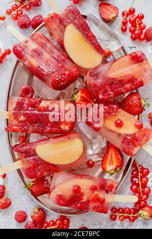 Pop-sicles faits maison à la framboise, à la fraise, aux pommes et au cassis sur une plaque de métal avec baies variées Banque D'Images