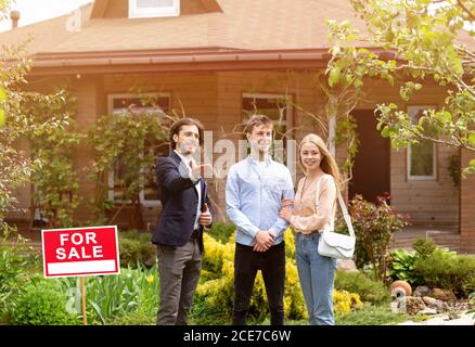 Jeune couple marié rencontre directeur immobilier pour regarder la maison à vendre, à l'extérieur Banque D'Images