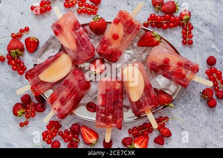 Pop-sicles faits maison à la framboise, à la fraise, aux pommes et au cassis sur une plaque de métal avec baies variées Banque D'Images