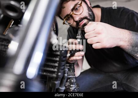 Un mécanicien de sexe masculin sérieux répare la bougie d'allumage sale de la moto travail en garage Banque D'Images