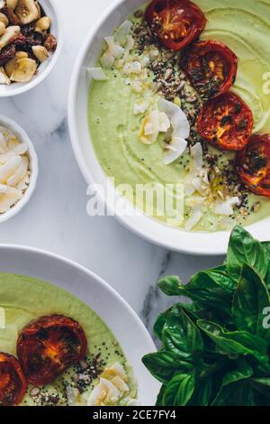 De dessus bols avec délicieux avocat et soupe à la crème de pomme décoration avec tomates séchées et noix de coco râpée grillée noix de cajou et basilic frais Banque D'Images