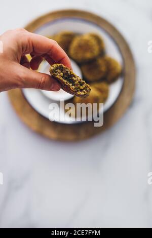 Vue de dessus de la main saisissant un falafel de lentille d'un plat servi avec une sauce au yaourt sur une table en bois Banque D'Images