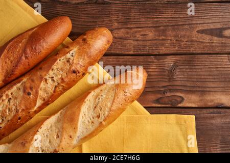 Trois baguettes françaises croustillantes sont des baguettes en tissu jaune serviette table en bois fond de baguettes en assortiment avec des graines de sésame Classic french pastri national Banque D'Images