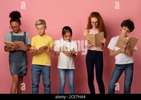 Divers enfants industriels lisant les manuels scolaires sur fond rose Banque D'Images