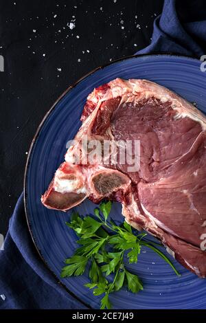 Steak de bœuf frais brut en forme de T avec poivron rouge, tomate, poivron rose et persil prêts à cuire. Pose à plat. Vue de dessus Banque D'Images