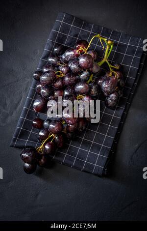 Vue de dessus d'un bouquet de délicieux raisins rouges mûrs placé sur une serviette à carreaux sur une surface noire Banque D'Images