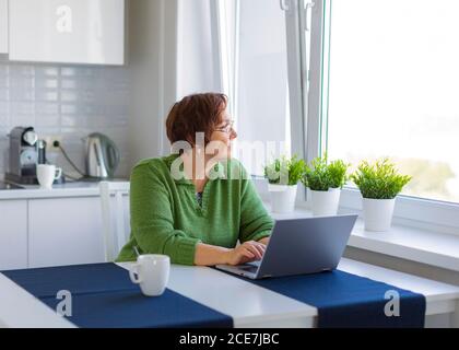 Femme sénior travaillant à domicile avec un ordinateur portable. Elle a bien réfléchi. Banque D'Images