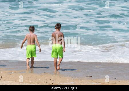 Deux jeunes garçons en vacances de vacances avec des shorts vert lime sur Fistral Beach à Newquay, en Cornouailles. Banque D'Images