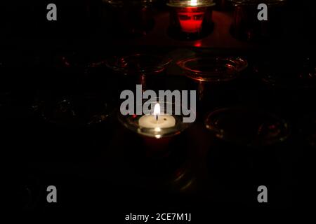 Gros plan de bougies allumées dans des pots en verre avec du rouge réflexion sur un arrière-plan sombre Banque D'Images