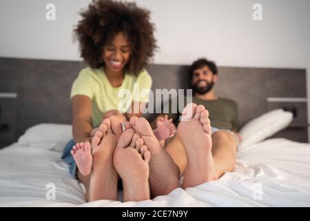 Contenu multiracial pieds nus mère et père couché sur le lit avec bébé mignon tout en appréciant le week-end ensemble