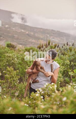 Ferme féminine calme avec de l'agneau mignon debout dans le champ vert par jour nuageux à la campagne Banque D'Images