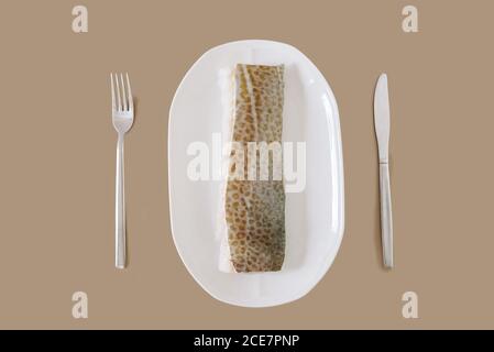 Vue de dessus de filet de poisson frais non cuit sur céramique blanche couteau de plaque et fourche sur fond beige Banque D'Images